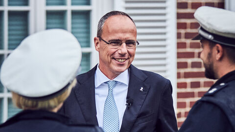 Minister Beuth im Gespräch mit einer Polizisten und einem Polizisten, die von hinten zu sehen sind.