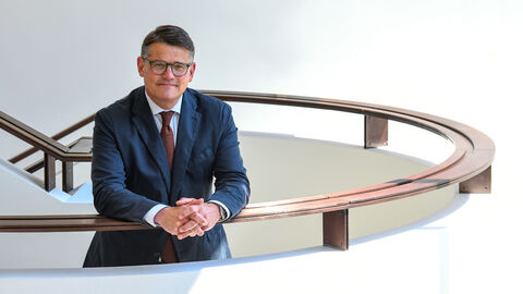 Boris Rhein steht auf einer geschwungenen Treppe, die Arme auf das Treppengeländer gelegt.