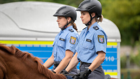 Zwei berittene Polizistinnen, jeweils auf einem Pferd sitzend, von der Seite fotografiert
