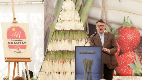 Ministerpräsident Rhein steht vor Publikum auf einer Bühne und hält eine Rede.