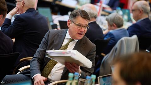 Ministerpräsident Boris Rhein sitzt auf einem Stuhl und hält Unterlagen in der Hand.