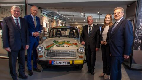 Fünf Menschen stehen in Businesskleidung um ein Auto herum.