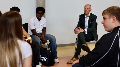 Jugendliche und ein Erwachsener sitzen in einem Kreis und unterhalten sich.