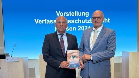 Roman Poseck und Bernd Neumann stehen nebeneinander und halten eine Broschüre in den Händen